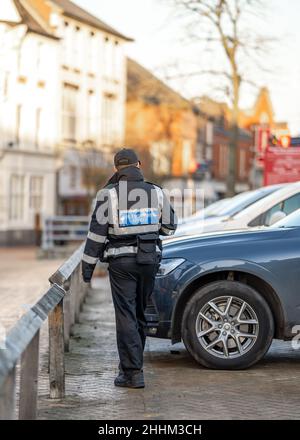 Un gardien de la circulation civile contrôle les voitures par un préposé au stationnement.Agent anonyme en uniforme regardant le parking pour les billets sur le pare-brise. Banque D'Images