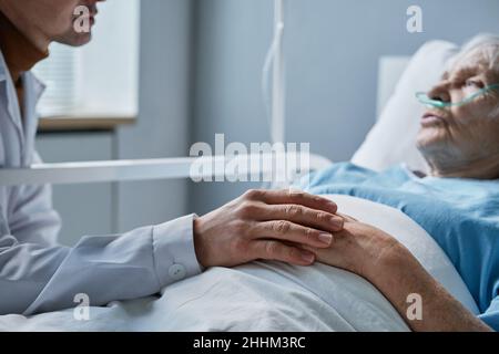 Gros plan d'un médecin tenant la main d'une femme âgée, allongé sur son lit, qui la soutient pendant sa maladie Banque D'Images