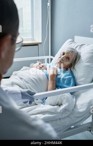 Femme sénior malade écoutant son médecin pendant qu'elle est allongée sur son lit à l'hôpital Banque D'Images