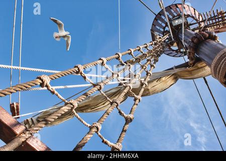 Truquage et mât d'un bateau à voile à l'ancienne avec un mouette volant contre un ciel bleu Banque D'Images