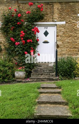 Marches menant à une porte blanche de chalet, partiellement entourée de roses rouges, village de Wadenhoe, Northamptonshire, Royaume-Uni Banque D'Images