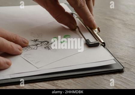 Les mains de l'homme appuient une feuille de papier avec un dessin dessiné à la main contre une tablette.Technique de dessin au stylo en pointillés.Dessin de fille avec des ballons verts sur papier Banque D'Images