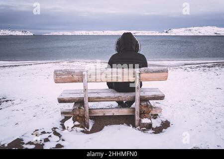 le vieil homme s'assoit seul sur un banc sur fond de baie. concept de solitude et de solitude.Paysage froid d'hiver.Un homme s'assoit seul et regarde le Banque D'Images