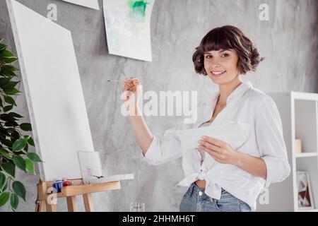 Photo portrait jeune fille portant chemise blanche gardant la brosse créant la peinture sur toile rester à la maison Banque D'Images