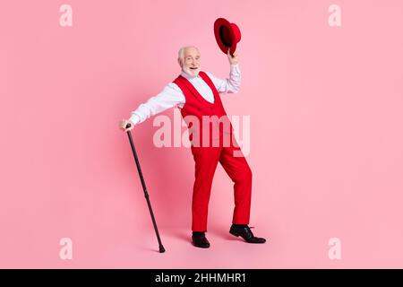 Photo pleine grandeur de l'homme beau âgé heureux positif sourire tenir chapeau bâton ont l'amusement isolé sur fond rose couleur Banque D'Images