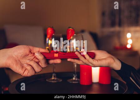 Saint-Valentin couple échanger des cadeaux avoir des boissons de vin pendant le dîner romantique célébrant à la maison avec des bougies allumées.Boîte cadeau rouge Banque D'Images
