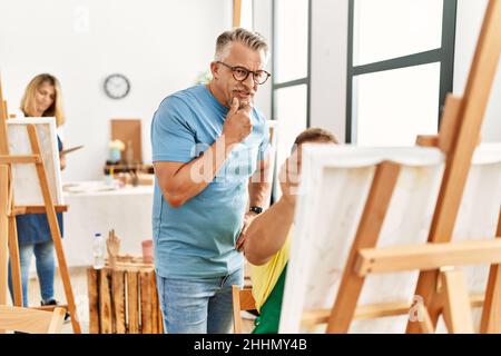 Groupe d'étudiants en peinture d'âge moyen qui dessinant au studio d'art. Professeur avec l'expression sérieuse regardant le dessin étudiant. Banque D'Images