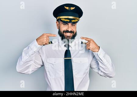 Jeune homme hispanique portant l'uniforme de pilote d'avion souriant gai montrant et pointant avec les doigts dents et la bouche. Concept de santé dentaire. Banque D'Images