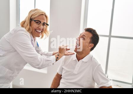 Homme et femme d'âge moyen médecin et patient examinant la gorge ayant une consultation médicale à la clinique Banque D'Images
