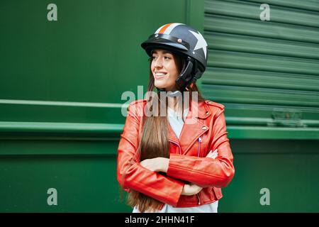 Jeune femme hispanique souriante heureuse portant un casque moto à la ville. Banque D'Images