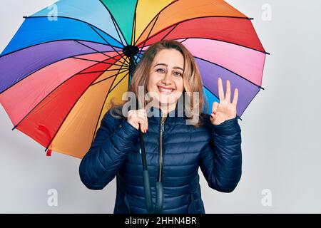 Moyenne âge femme caucasienne tenant un parapluie coloré faisant signe ok avec les doigts, souriant sympathique gesturant excellent symbole Banque D'Images