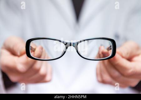 Un opticien en manteau blanc montre une paire de lunettes correctrices pour corriger la myopie.Les lunettes ont un cadre noir. Banque D'Images