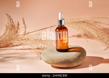 Huile essentielle sur une pierre de galet de rivière sur un fond beige.Produit de beauté médical cosmétique en bouteille de verre brun avec une pipette pour l'aromathérapie, al Banque D'Images