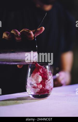 Gros plan vertical d'une boisson rouge versée dans un verre avec de la glace sur une table blanche Banque D'Images