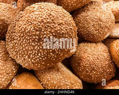 Gros plan d'une pile de petits pains de hamburger fraîchement cuits parsemés de graines de sésame. Banque D'Images