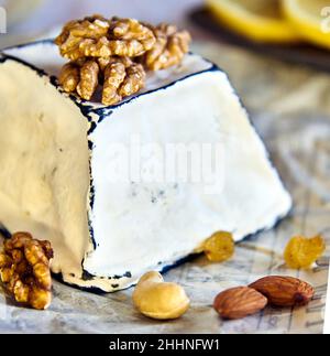 Fromage en moule blanc avec bords noirs de charbon de bois, noix et raisins secs, sur papier d'emballage. Banque D'Images