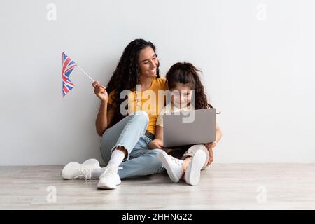 École de langue en ligne.Mère et fille utilisant un ordinateur portable et tenant le drapeau britannique Banque D'Images