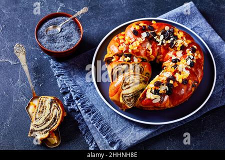 Pain brioche braisé aux graines de pavot, parsemé de morceaux d'orange confits, de raisins secs et d'amandes pelées en tranches sur une assiette de béton Banque D'Images