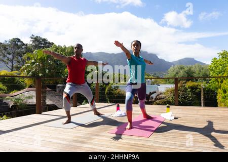 Le jeune couple afro-américain pratiquant le guerrier pose ensemble sur la terrasse le jour ensoleillé. Les gens et le concept de mode de vie sain, inchangé. Banque D'Images