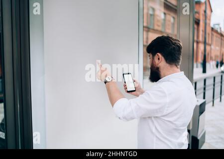 Homme barbu sans visage comparant les informations du smartphone sur un tableau blanc Banque D'Images