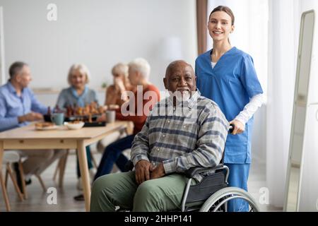 Patiente âgée heureuse en fauteuil roulant avec une infirmière féminine Banque D'Images