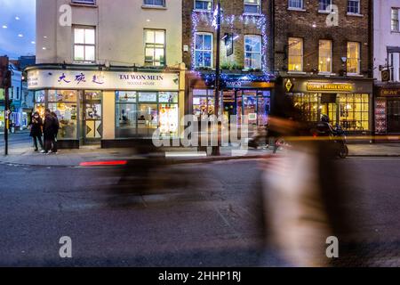 Vue nocturne de Church Street Greenwich Town Center avec des gens passant devant et des traînées floues de la circulation en mouvement, 30th décembre 2021 Banque D'Images