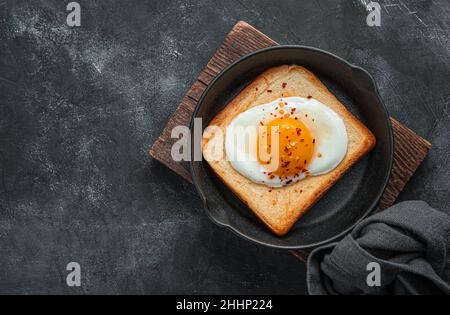 Petit déjeuner frais avec œufs frits dans une poêle sur fond sombre. Banque D'Images