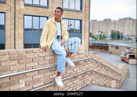 Homme avec caméra assis sur un mur de briques dans la rue Banque D'Images