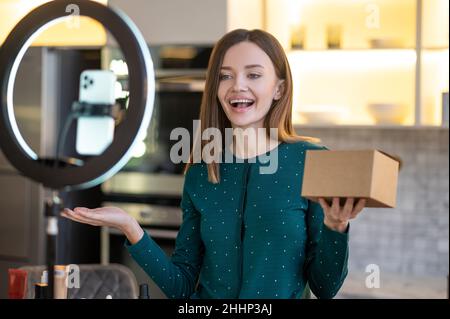 Jeune entraîneur souriant de beauté présentant de nouveaux produits de beauté à l'auditoire en ligne Banque D'Images