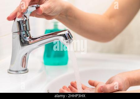 Maman aide l'enfant à se laver les mains sous l'eau courante du robinet dans le lavabo à la maison dans la salle de bains.Mise au point sélective.Gros plan Banque D'Images