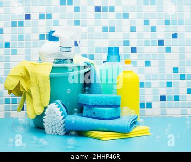 Nettoyants et détergents dans un seau, accessoires de nettoyage, fond bleu avec bulles de savon Banque D'Images