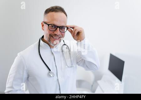 Portrait d'un médecin souriant en uniforme médical blanc, stéthoscope et lunettes regarder l'appareil photo Banque D'Images