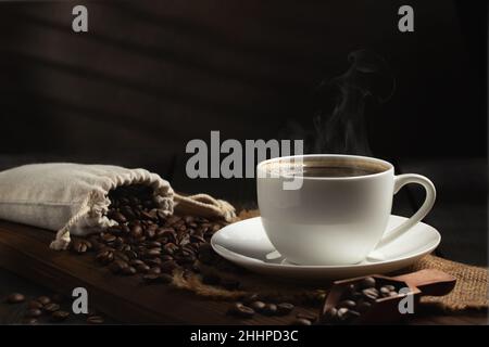 Tasse blanche de café chaud frais et de grains de café sur table en bois. Banque D'Images