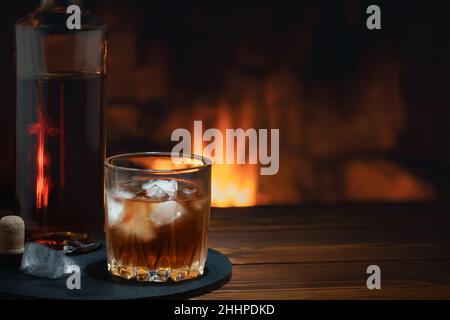 Bouteille et verre de whisky avec glace sur la table près de la cheminée. Concept repos et détente Banque D'Images