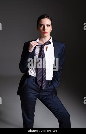 Jeune femme européenne en costume d'homme noir isolé sur gris foncé Banque D'Images