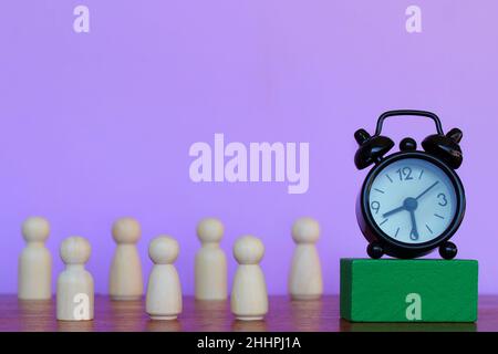 Heures de travail, salaire horaire, concept de date limite.Réveil et poupées en bois sur fond violet. Banque D'Images