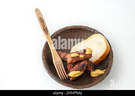 Roulés de viande hachés roumains, mici ou mititei sur un bol en bois sculpté avec de la moutarde et une fourchette traditionnelle en bois, isolée sur fond blanc Banque D'Images