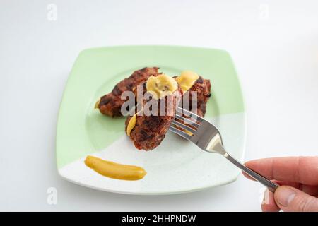 MICI ou mititei (cuisine roumaine traditionnelle) avec moutarde sur une plaque en céramique, sur fond blanc.Main tenant une fourche en acier inoxydable Banque D'Images