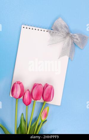 Tulipes roses avec bloc-notes avec noeud argenté et place pour le texte sur fond bleu pâle.Vacances, 8 mars, anniversaire, International Women's and Mother's da Banque D'Images