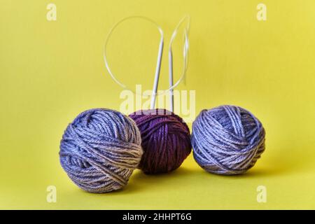 Composition de trois boules violettes de fil et aiguilles circulaires en bois sur fond jaune. Banque D'Images