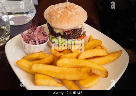 Bœuf juteux à l'intérieur d'une pile de burgers gastronomiques sur une assiette blanche avec de grosses frites et un petit plat de coleslaw. Banque D'Images