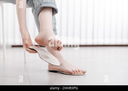 Femme à l'intérieur de la semelle intérieure orthopédique, gros plan.Fille tenant une semelle à côté du pied à la maison.Semelles intérieures orthopédiques.Bannière de soins des pieds.Pieds plats Banque D'Images