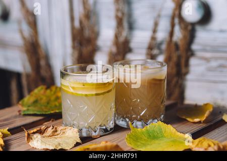 Gros plan de deux verres de boisson chaude à la poire, entourée de feuilles d'automne Banque D'Images