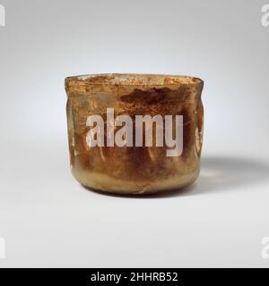 Coupelle en verre avec bords indentés 1st–2nd Century A.D. incolore romain avec une teinte verdâtre pâle.jante irrégulière, légèrement renflée sous le bord; côtés verticaux, arrondis à la base; fond presque plat.une rainure horizontale découpée à la roue sur le col; douze indentations verticales sur les côtés.intact; bulles pincées;légère piqûre, mais la plupart des surfaces couvertes d'un épais vernis crémeux et d'une brillante irissidence.Coupelle en verre avec côtés en retrait 239806 Banque D'Images