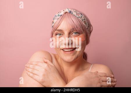 Belle femme appliquant le rose sous les cellules oculaires pour les cercles sombres et puffiness regardant la caméra isolée sur fond rose.Cosmétique ca Banque D'Images