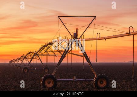 Déplacement latéral système d'irrigation agricole sur le champ labouré au coucher du soleil, équipement agricole pour l'arrosage des terres agricoles cultivées Banque D'Images