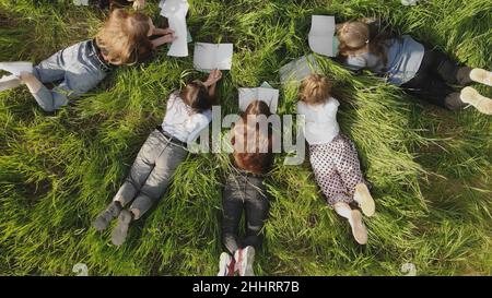 Les jeunes filles s'étendent sur l'herbe dans un parc de la ville avec des carnets. Banque D'Images