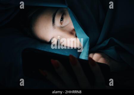 Une jeune femme utilise le téléphone cellulaire la nuit.L'écran du téléphone brille dans le visage. Banque D'Images