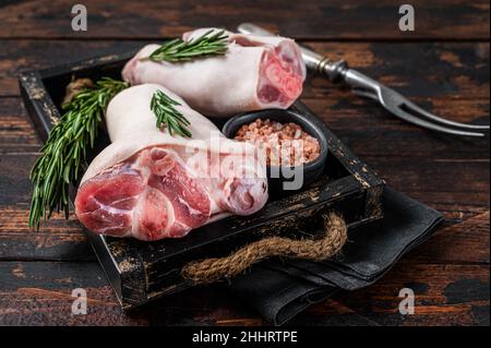 Jarret de porc cru non cuit, porte-fusée, pieds dans un plateau en bois avec des herbes.Arrière-plan en bois.Vue de dessus Banque D'Images