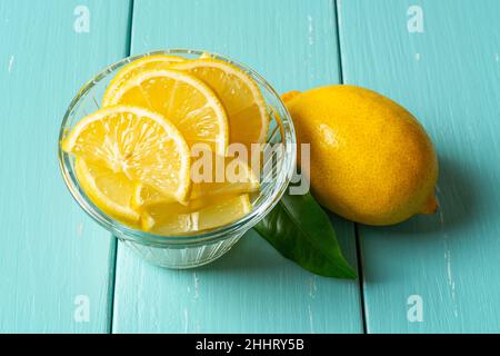 Des tranches de citron crues dans un bol en verre et un fruit entier sur une table en bois turquoise.Agrumes jaunes coupés frais pour les concepts de vitamine C, antioxydant. Banque D'Images